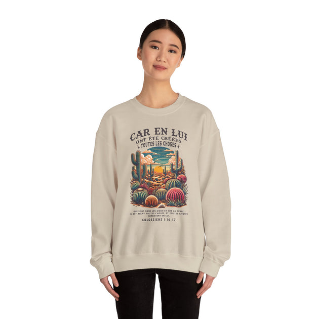 Une femme porte un sweatshirt beige illustré d'un paysage désertique et d'un verset biblique.