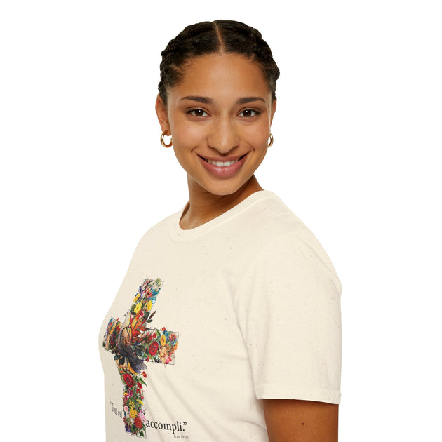 Une femme porte un t-shirt beige orné d'une croix fleurie avec l'inscription Tout est accompli.
