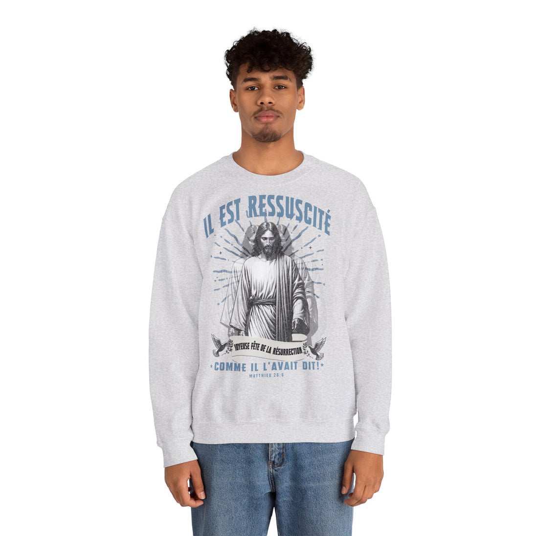 Un homme porte un sweatshirt gris chiné avec une illustration religieuse et le texte Il est ressuscité.