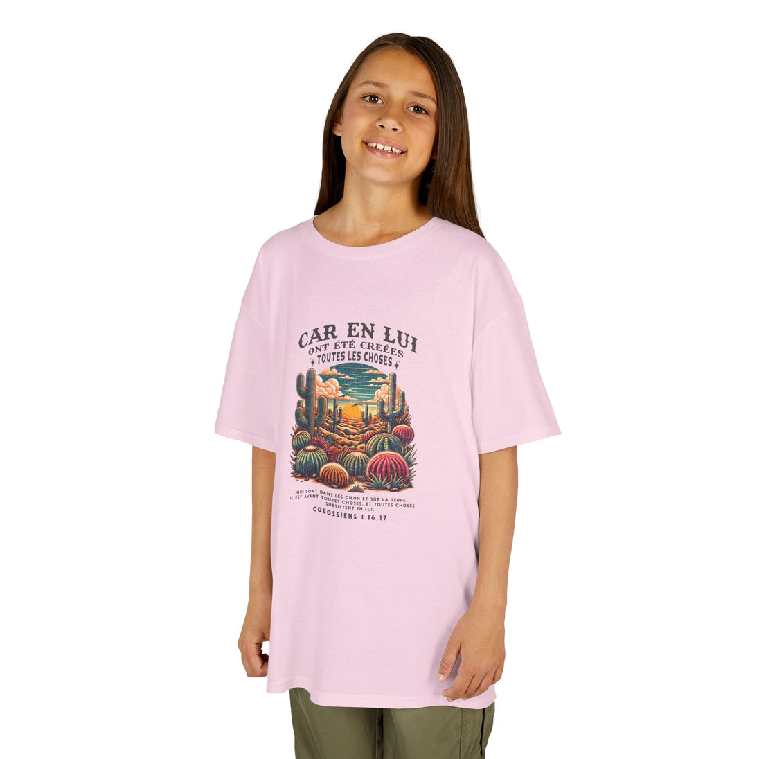 Une jeune fille porte un t-shirt rose en coton avec une illustration de désert et un texte biblique.
