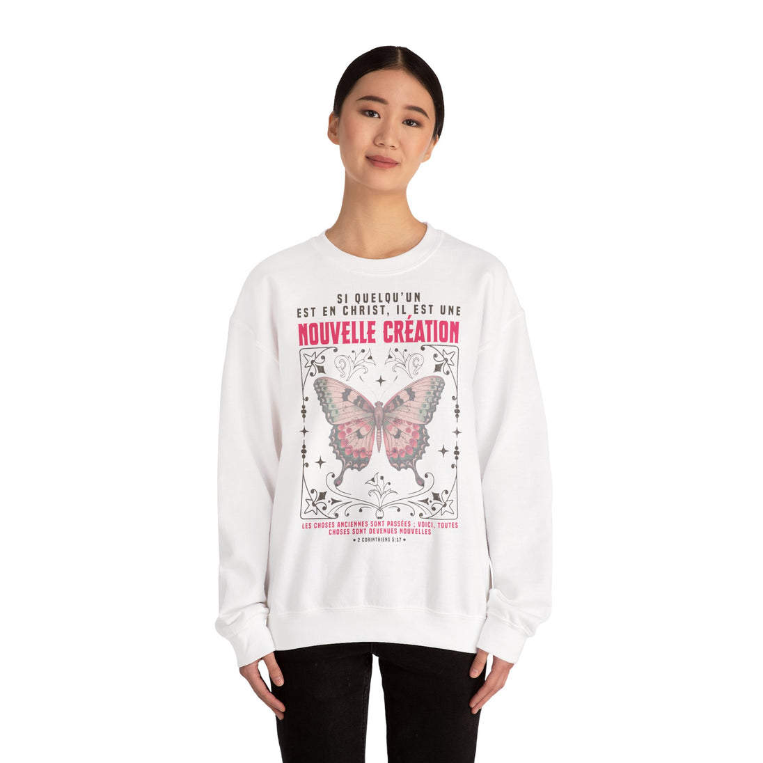 Une femme porte un sweat-shirt blanc avec un papillon et un texte biblique en français.
