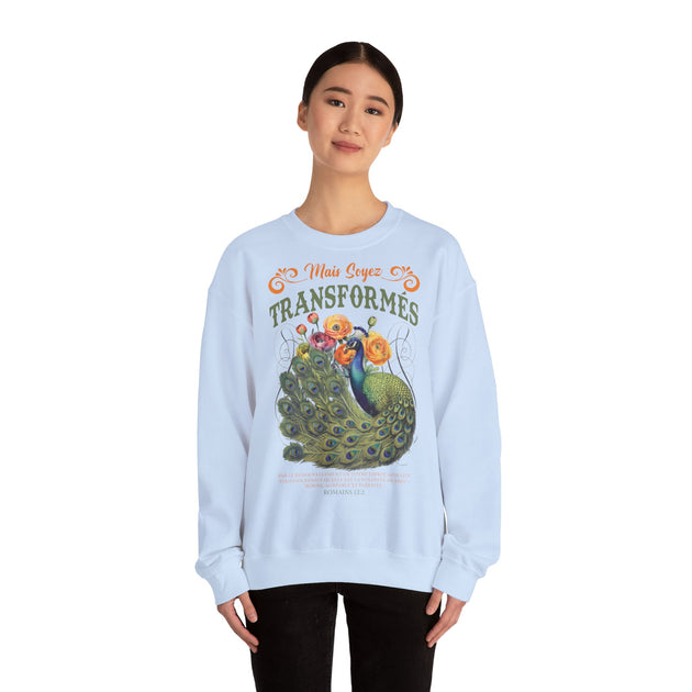 Une femme porte un sweat-shirt blanc avec une illustration de paon et le texte Mais soyez transformés.