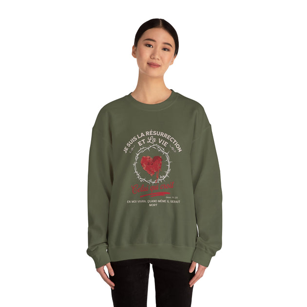 Une femme porte un sweat-shirt vert olive avec un motif de cœur couronné d'épines et du texte.