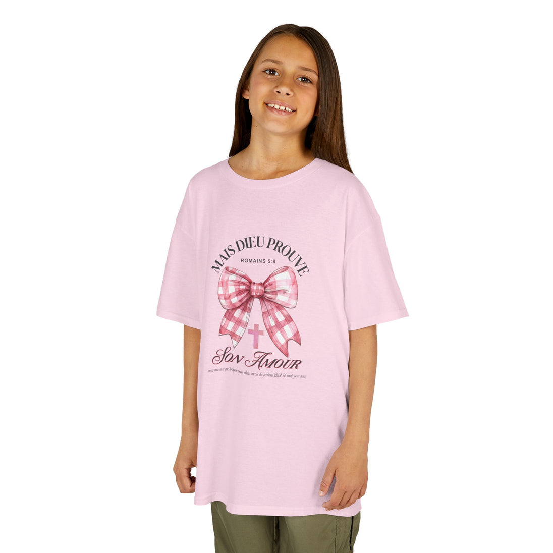 Une jeune fille porte un t-shirt rose orné d'un nœud vichy et d'une croix avec un texte religieux.