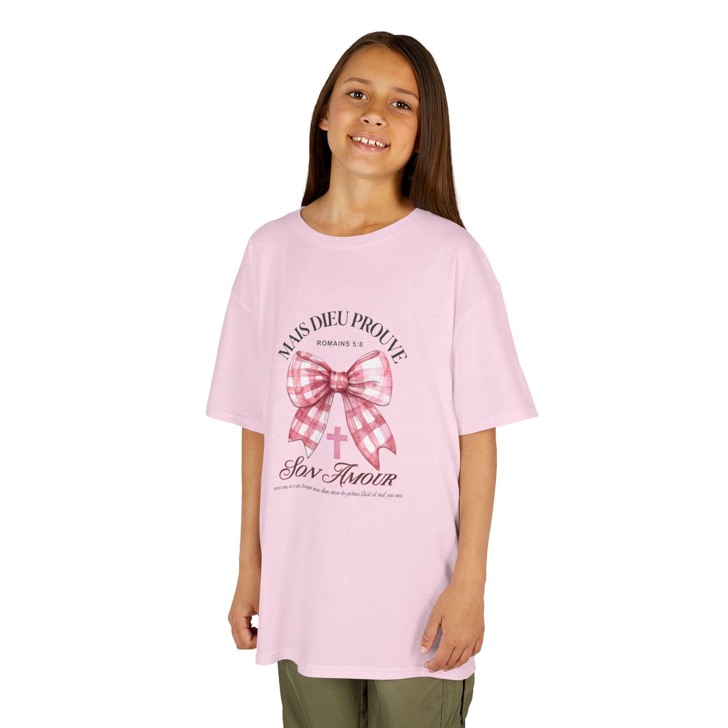 Une jeune fille porte un t-shirt rose orné d'un nœud vichy et d'une croix avec un texte religieux.