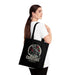 Une femme porte un tote bag noir en coton biologique orné d'un corbeau et de roses.