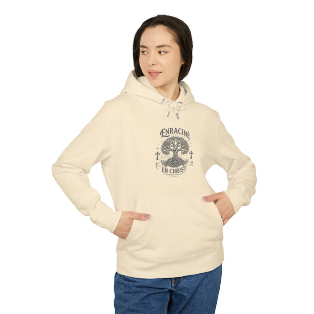 Une femme porte un sweat à capuche beige avec un motif d'arbre et le texte Enraciné en Christ.