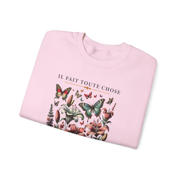 Sweatshirt rose pâle plié avec une illustration de fleurs et papillons et le texte Il fait toute chose.