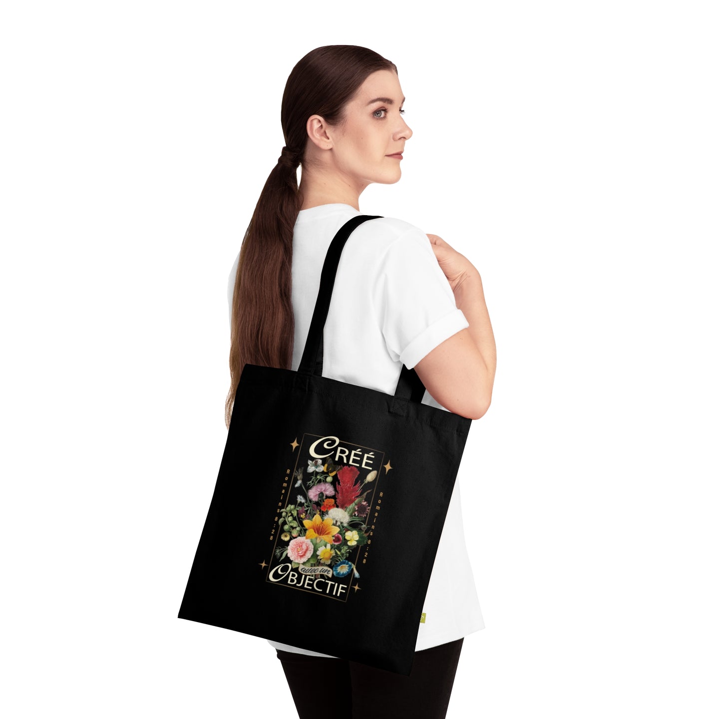Une femme porte sur l'épaule un sac fourre-tout noir en coton orné d'un motif floral et du texte.