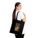 Une femme porte sur l'épaule un sac fourre-tout noir en coton orné d'un motif floral et du texte.