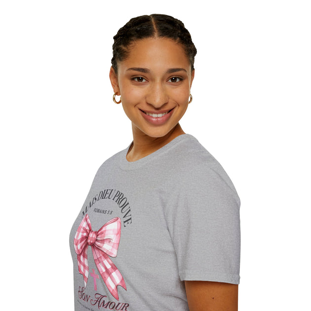 Une femme porte un t-shirt gris orné d'un nœud rose à carreaux et du texte religieux.