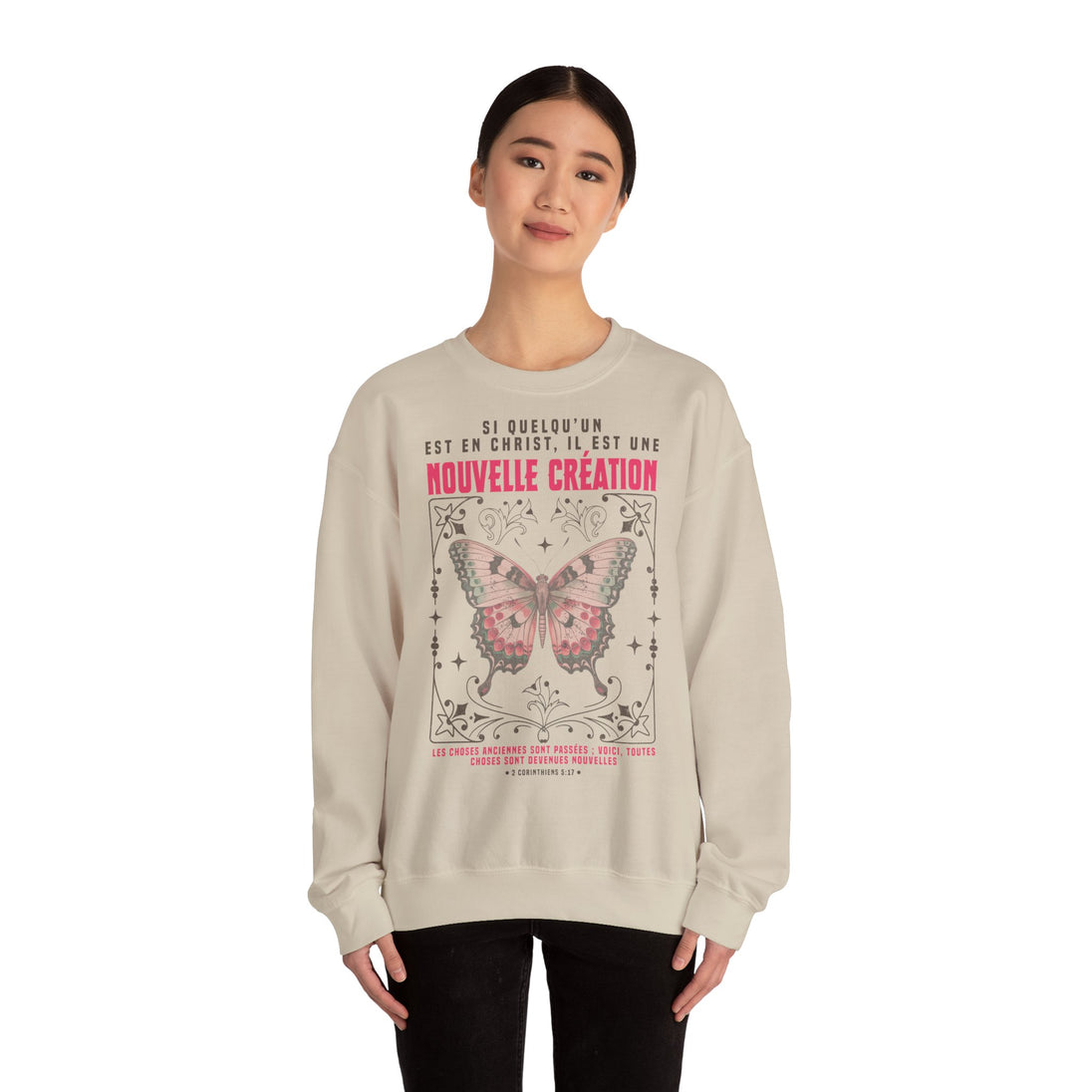 Une femme porte un sweat-shirt beige orné d'un papillon et d'un verset biblique en français.