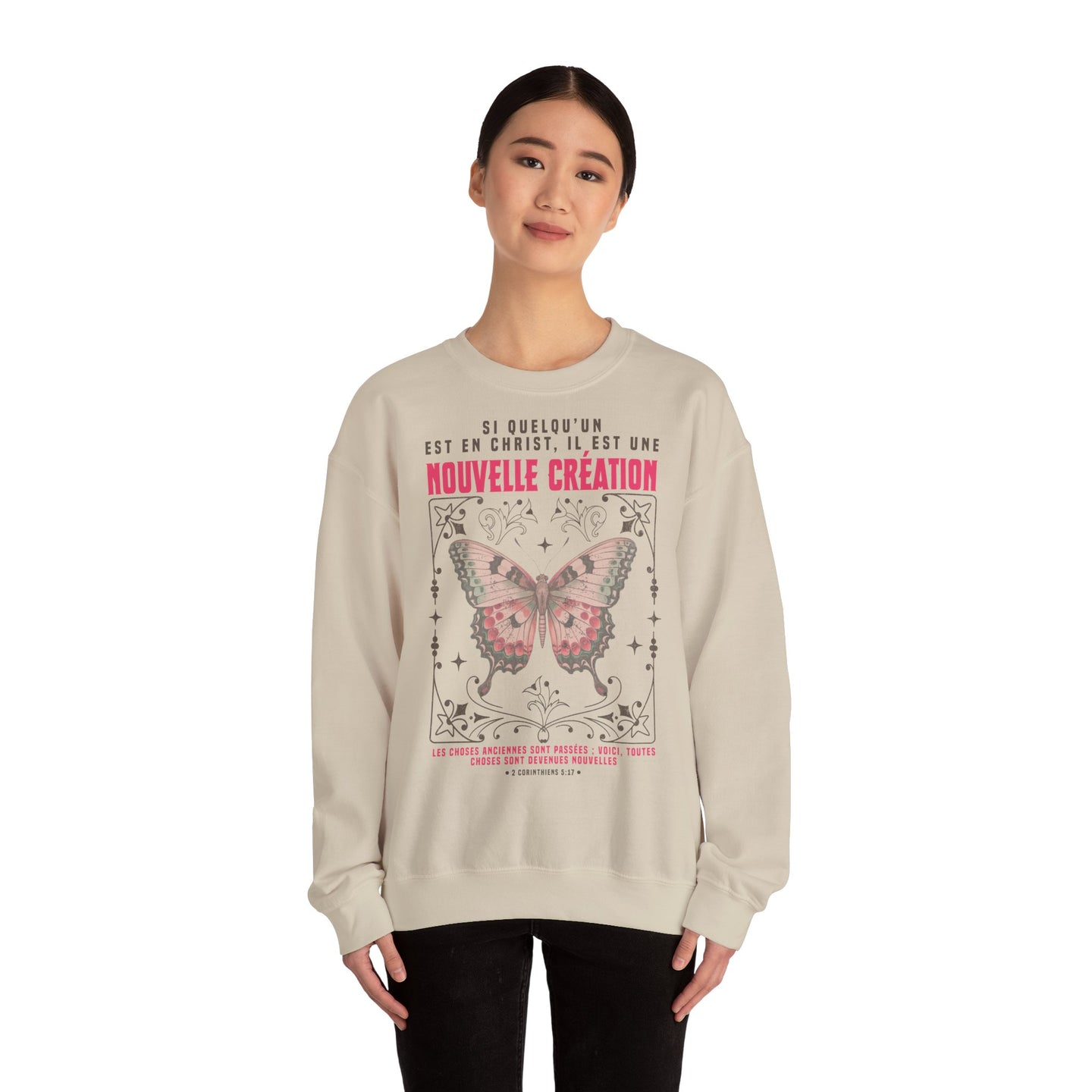 Une femme porte un sweat-shirt beige orné d'un papillon et d'un verset biblique en français.