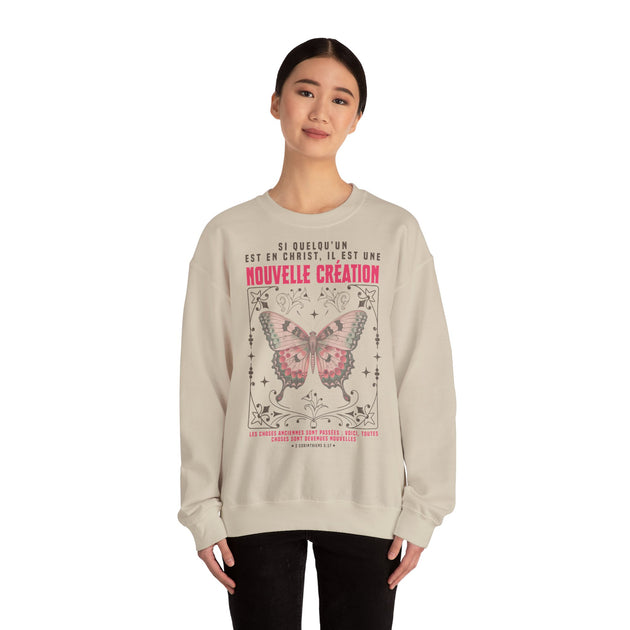 Une femme porte un sweat-shirt beige orné d'un papillon et d'un verset biblique en français.
