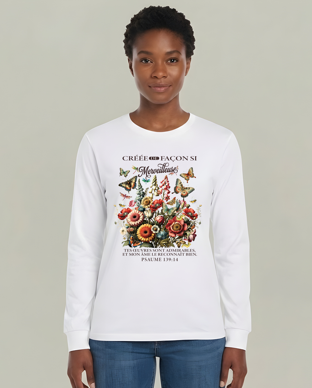 Une femme porte un t-shirt blanc à manches longues orné d'un motif floral et d'un verset biblique.