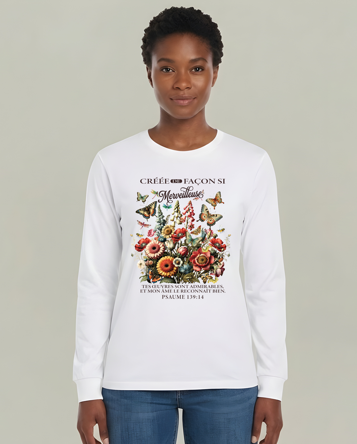 Une femme porte un t-shirt blanc à manches longues orné d'un motif floral et d'un verset biblique.
