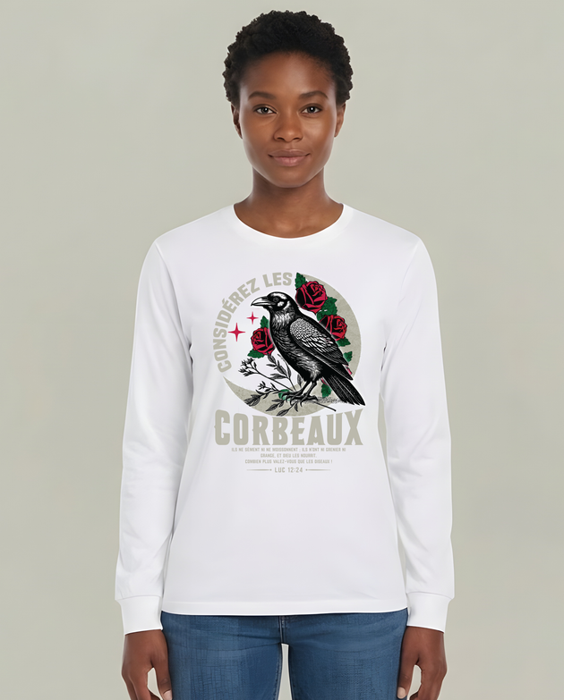 Femme portant un t-shirt blanc à manches longues avec corbeau, roses et texte biblique Luc 12:24.
