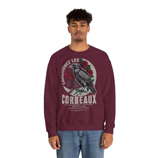 Un homme porte un sweatshirt bordeaux avec une illustration de corbeau et le texte Luc 12:24.