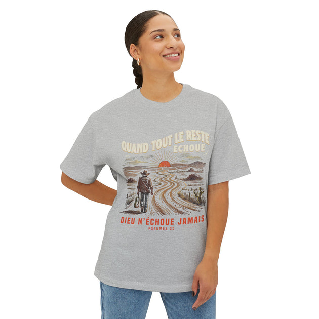 Une femme porte un t-shirt gris oversize avec une illustration de voyageur et un texte religieux.
