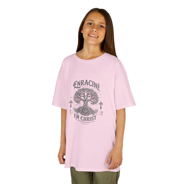 Une jeune fille porte un t-shirt rose clair avec un motif d'arbre et le texte Enraciné en Christ.