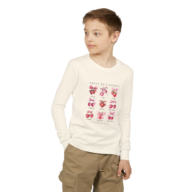 Un enfant porte un t-shirt à manches longues blanc orné d'un motif de fruits et de texte.