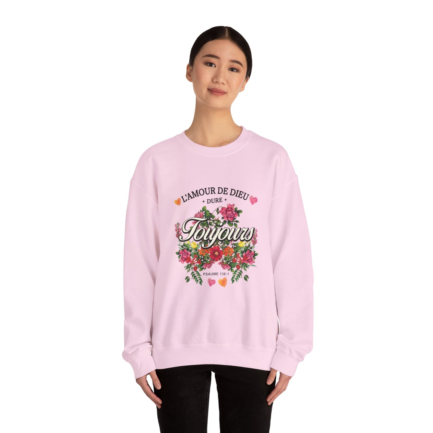 Une femme porte un sweatshirt rose pâle orné d'un motif floral et du texte L'Amour de Dieu.