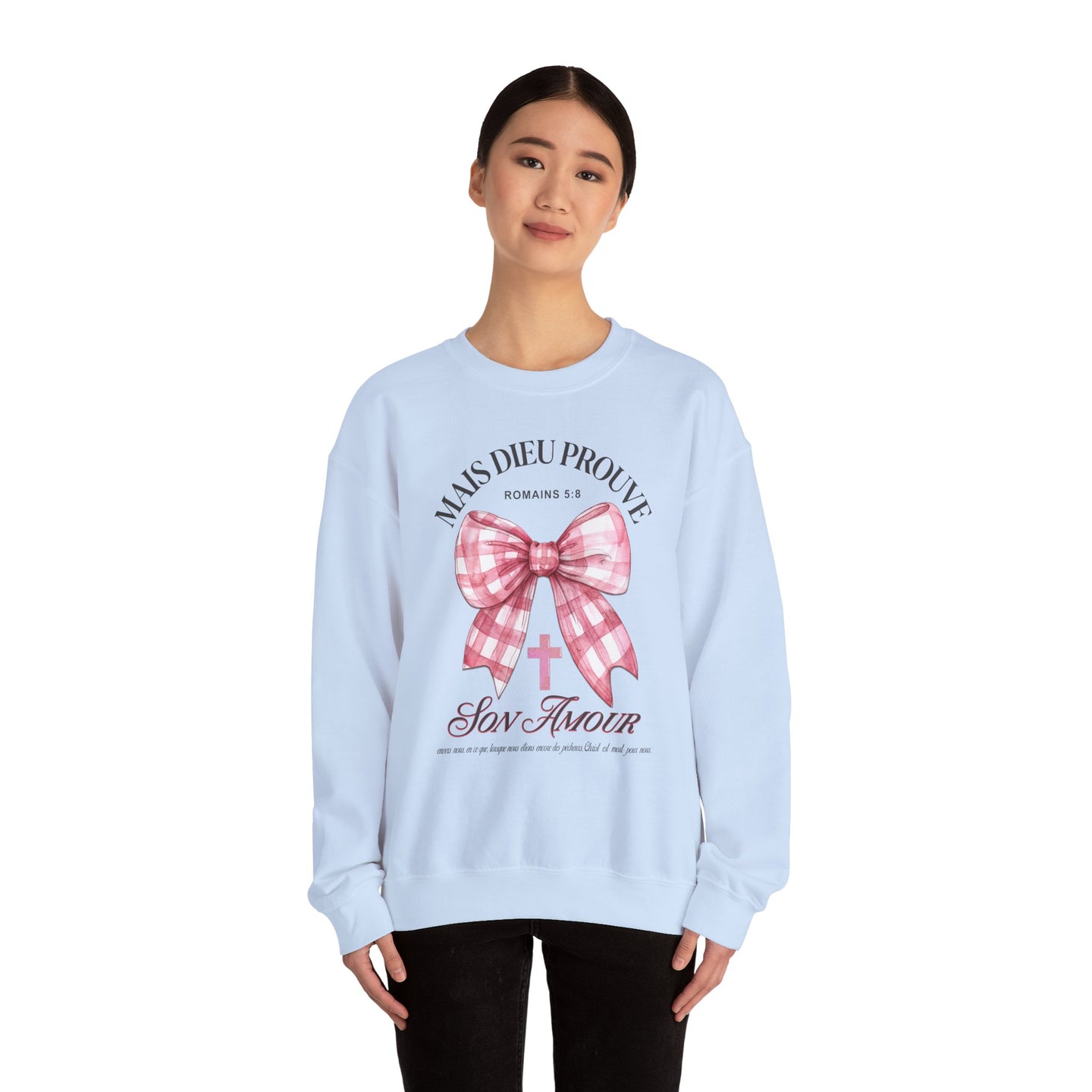 Une femme porte un sweat-shirt bleu clair avec un motif de nœud rose et une croix chrétienne.
