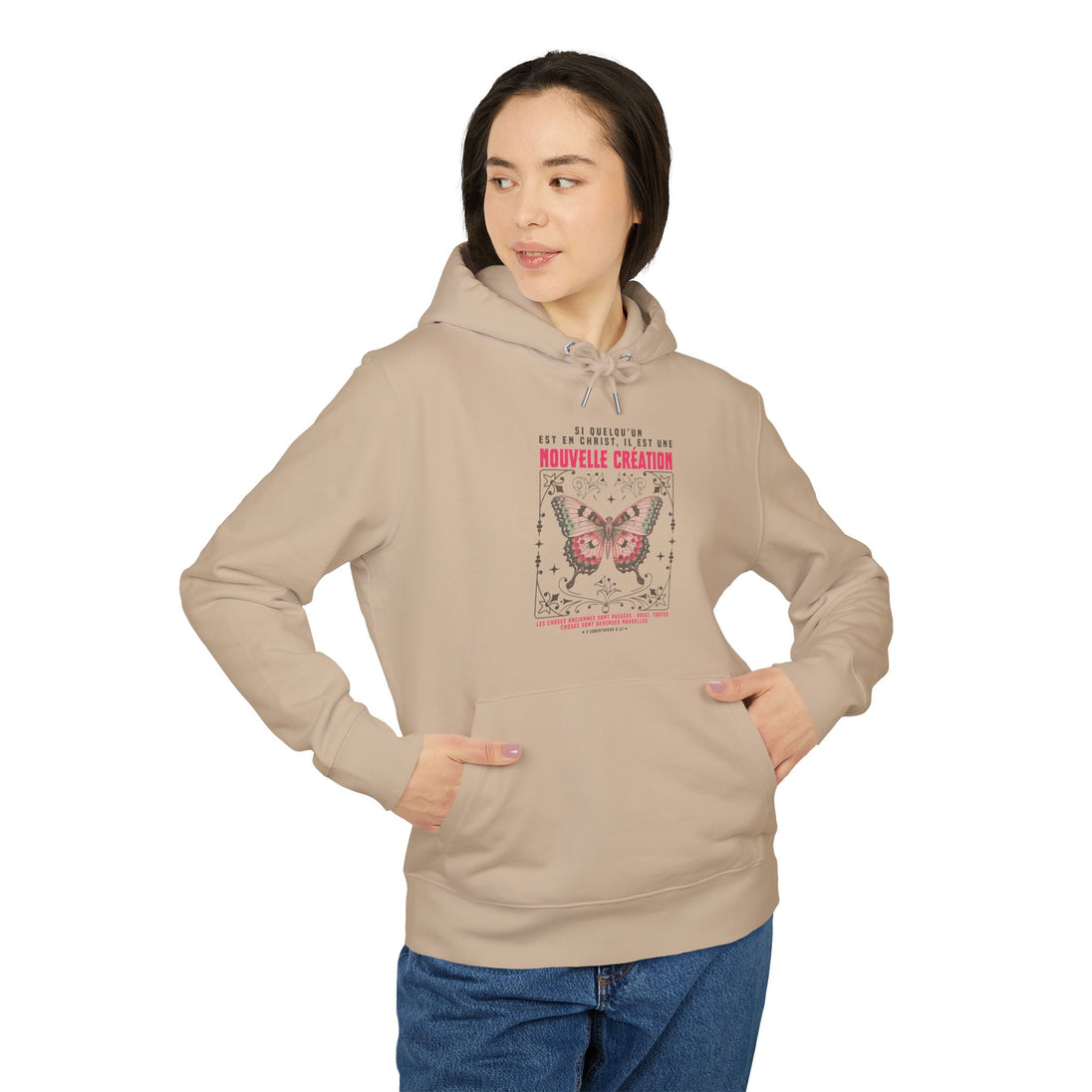 Une femme porte un sweat à capuche beige avec un motif de papillon et un texte religieux.