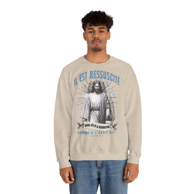 Un homme porte un sweatshirt beige avec une illustration religieuse et le texte Il est ressuscité.