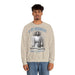 Un homme porte un sweatshirt beige avec une illustration religieuse et le texte Il est ressuscité.