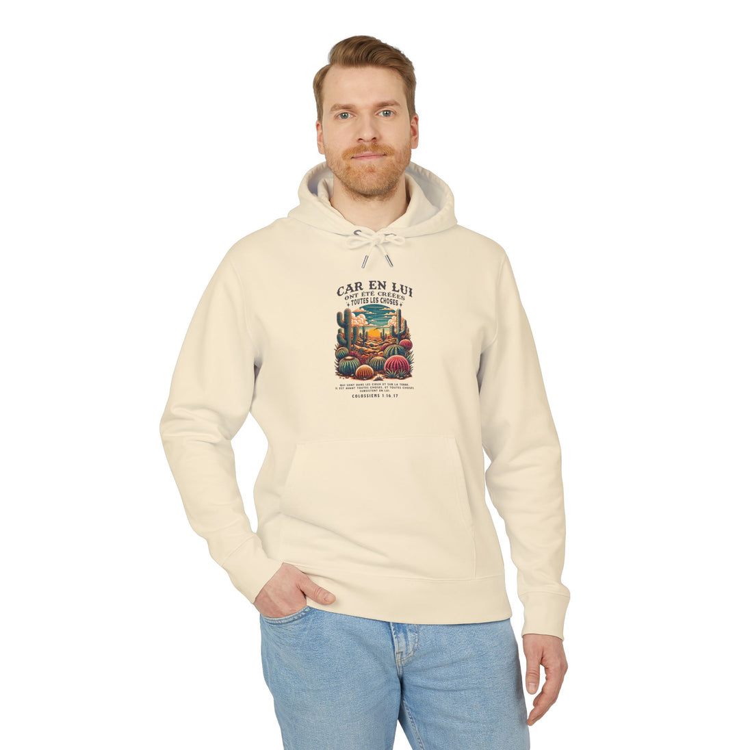 Un homme porte un sweat à capuche beige avec une illustration de désert et un verset biblique.
