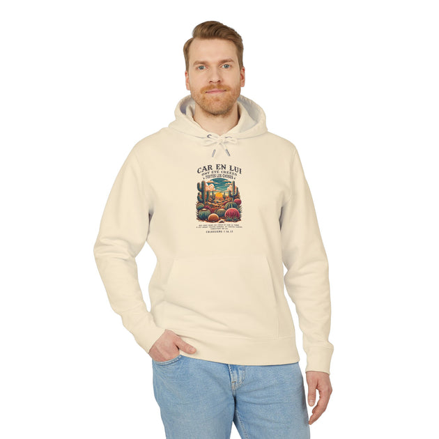 Un homme porte un sweat à capuche beige avec une illustration de désert et un verset biblique.