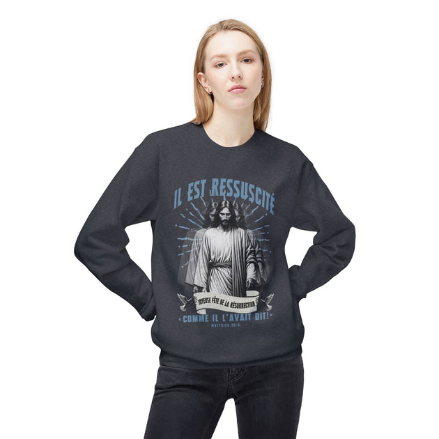 Une femme porte un sweatshirt gris foncé avec une illustration religieuse et le texte Il est ressuscité.