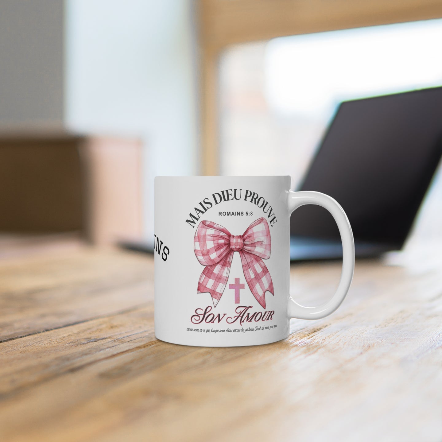 Mug blanc en céramique orné d'un nœud rose à carreaux, d'une croix et du verset Romains 5:8.