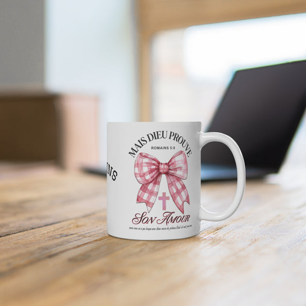 Mug blanc en céramique orné d'un nœud rose à carreaux, d'une croix et du verset Romains 5:8.