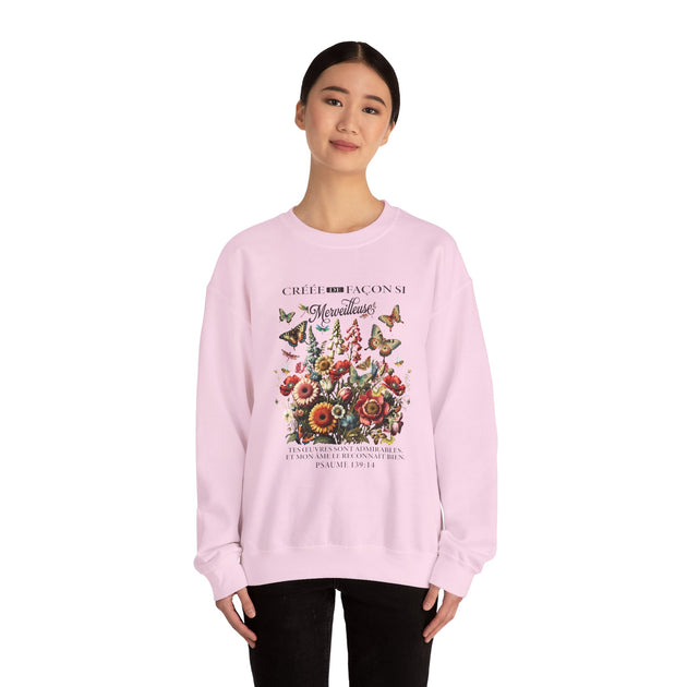 Une femme porte un sweat-shirt rose pâle orné d'un motif floral et de papillons avec un texte religieux.