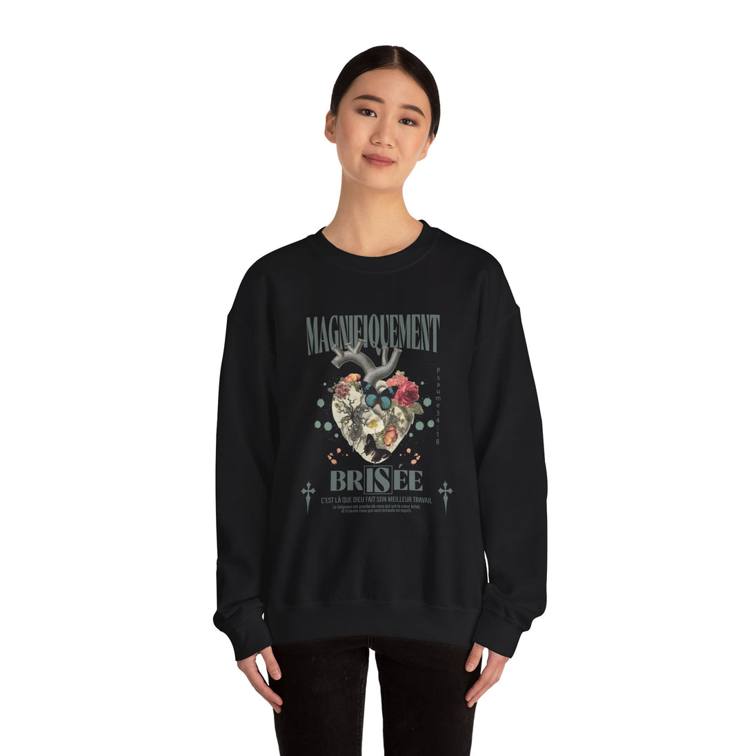 Une femme porte un sweat-shirt noir avec un motif de cœur floral et le texte Magnifiquement Brisée.