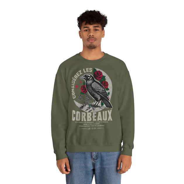 Un homme porte un sweatshirt vert olive orné d'une illustration de corbeau et de texte biblique.