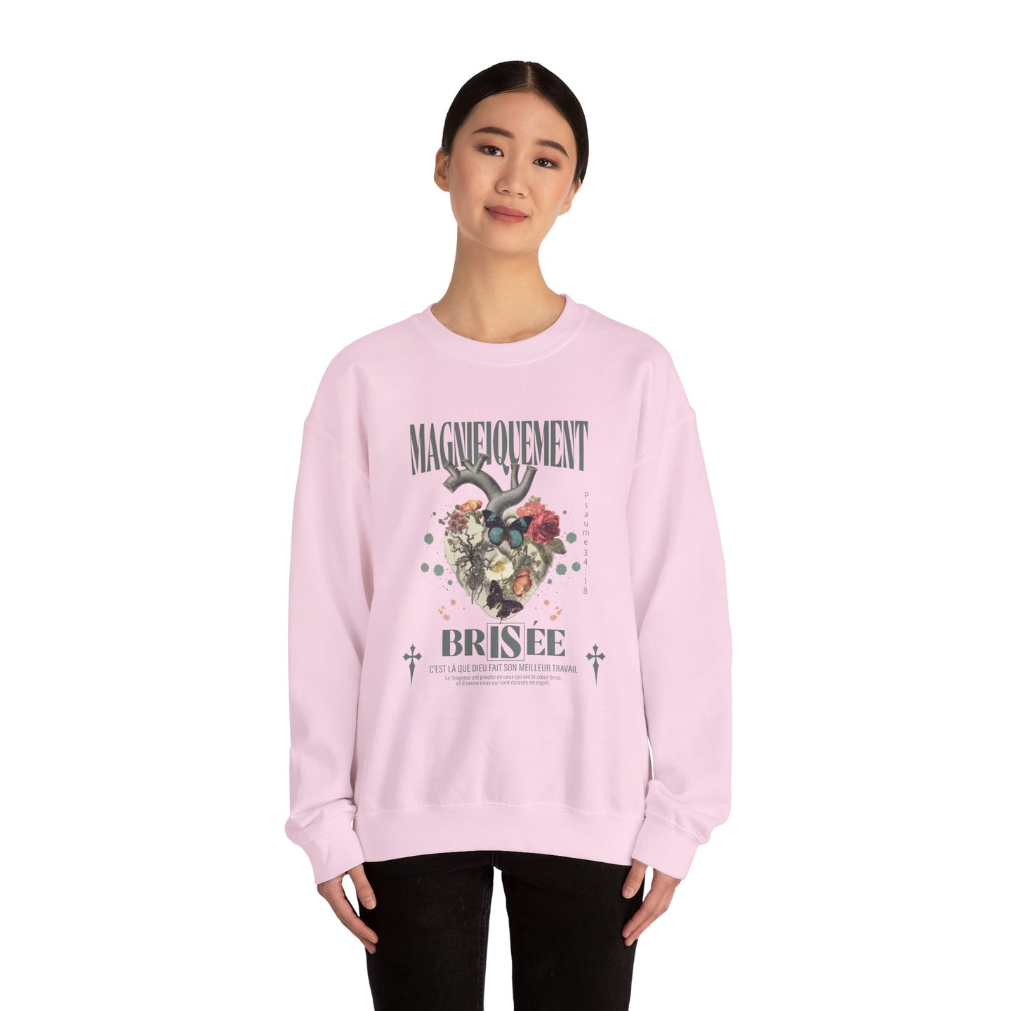 Une femme porte un sweat-shirt rose pâle orné d'un motif de cœur floral et du texte Magnifiquement Brisée.
