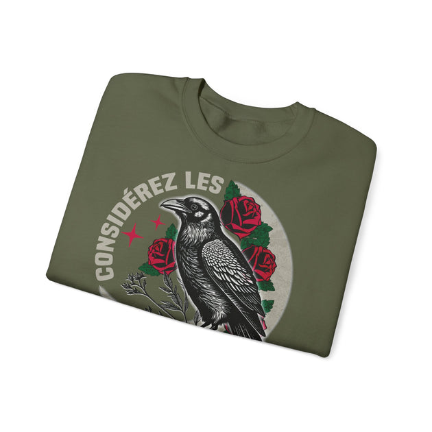 Sweat-shirt vert olive plié avec une illustration de corbeau et de roses et le texte Considérez les.