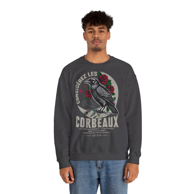 Un homme porte un sweatshirt gris anthracite orné d'un corbeau et du texte Luc 12:24.