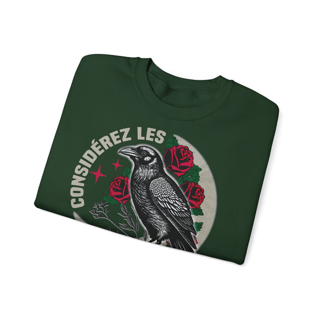 Sweat-shirt vert foncé plié avec une illustration de corbeau, de roses et le texte Considérez les.