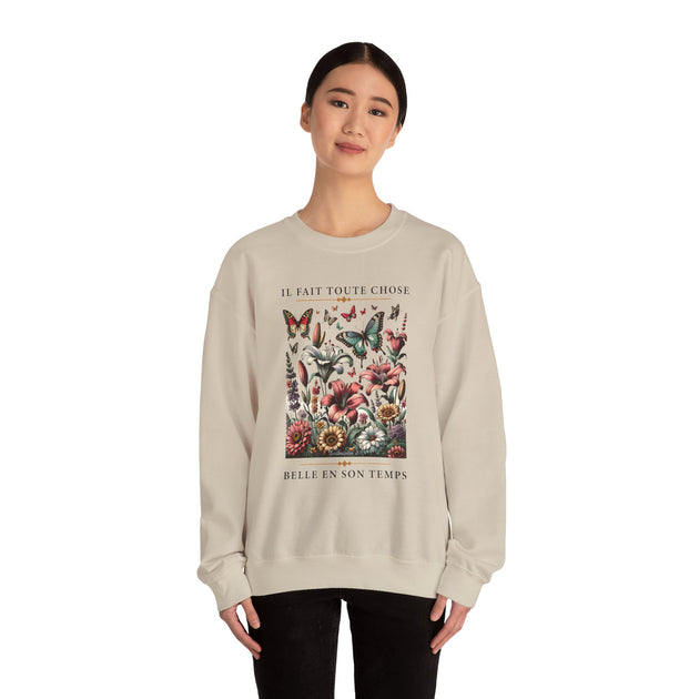 Une femme porte un sweatshirt beige orné d'un motif floral et de papillons avec une inscription.