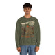 Un homme porte un sweatshirt vert olive avec une illustration de cow-boy et un message religieux.
