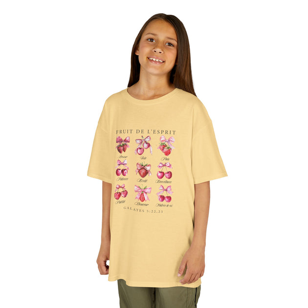 Une jeune fille porte un t-shirt jaune pâle illustré de fruits et de nœuds roses.