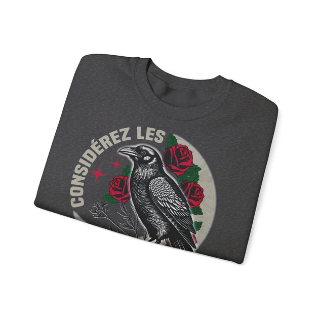 Sweat-shirt gris foncé plié avec une illustration de corbeau et de roses et le texte Considérez les.