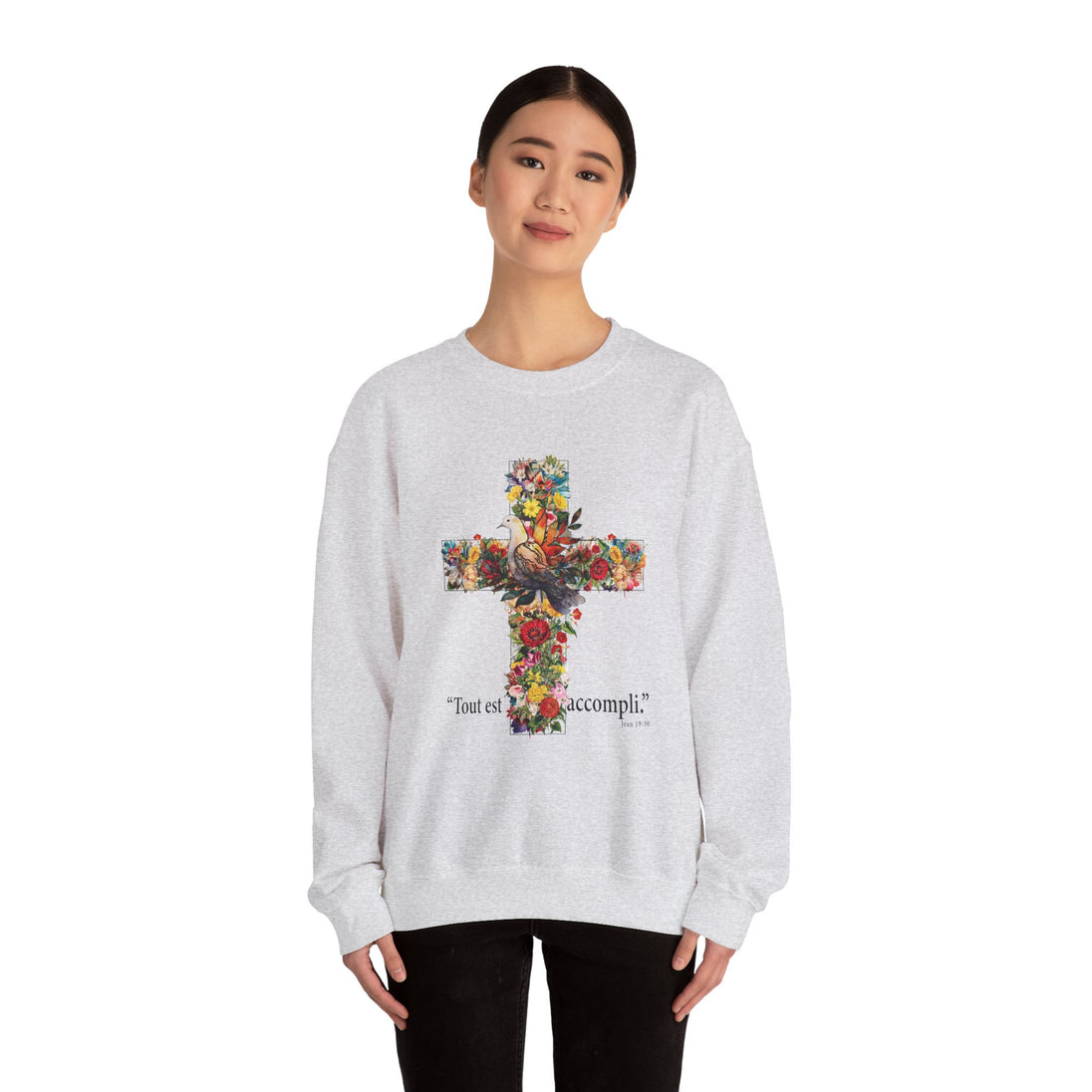 Une femme porte un sweat-shirt gris chiné orné d'une croix florale et de l'inscription Tout est accompli.