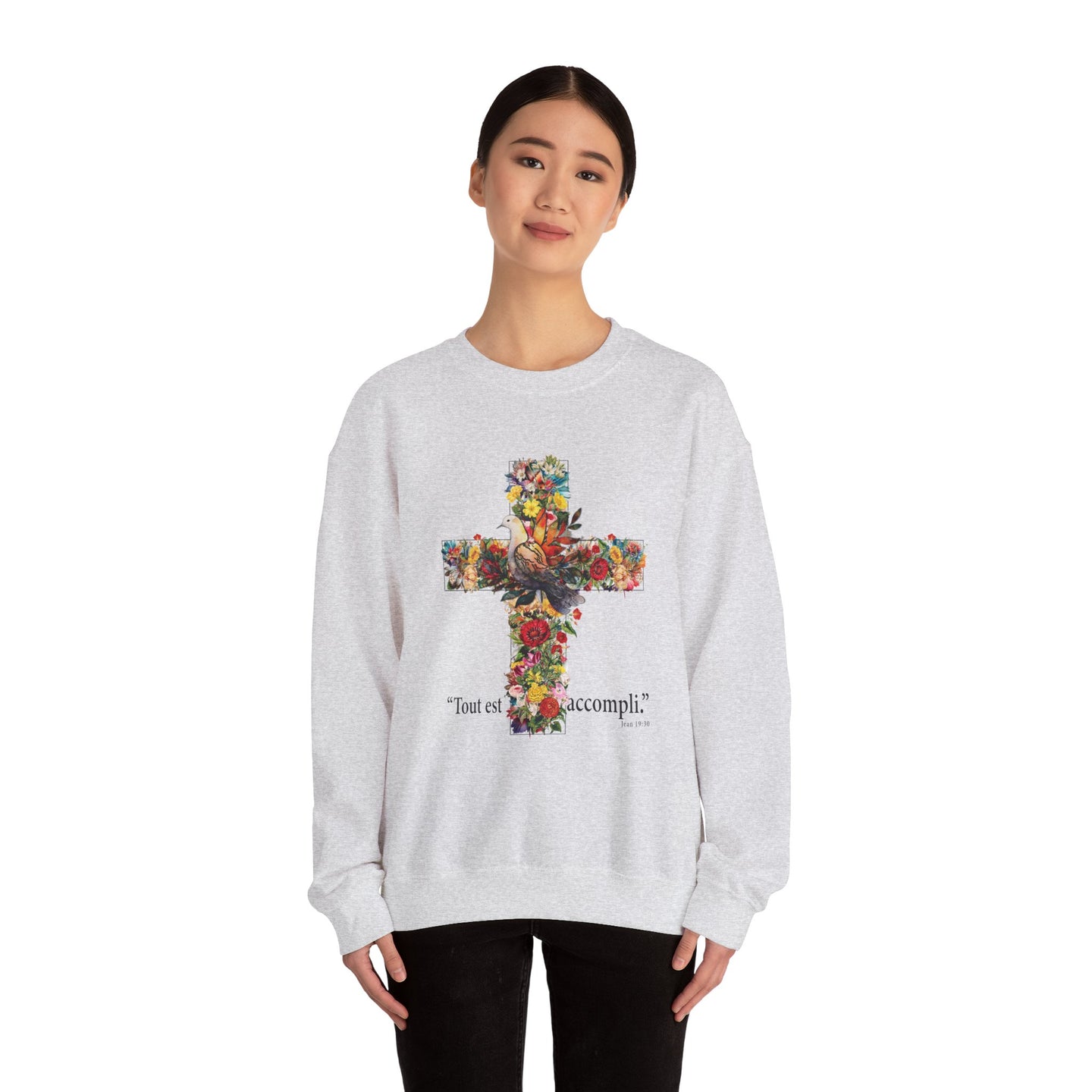 Une femme porte un sweat-shirt gris chiné orné d'une croix florale et de l'inscription Tout est accompli.