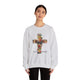 Une femme porte un sweat-shirt gris chiné orné d'une croix florale et de l'inscription Tout est accompli.