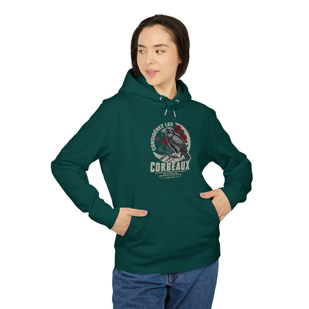 Une femme porte un sweat à capuche vert foncé avec une illustration de corbeau et des roses.